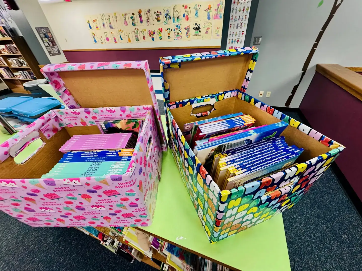 Two decorated Birthday Boxes, stocked with brand-new books in English and Spanish, on a school library table