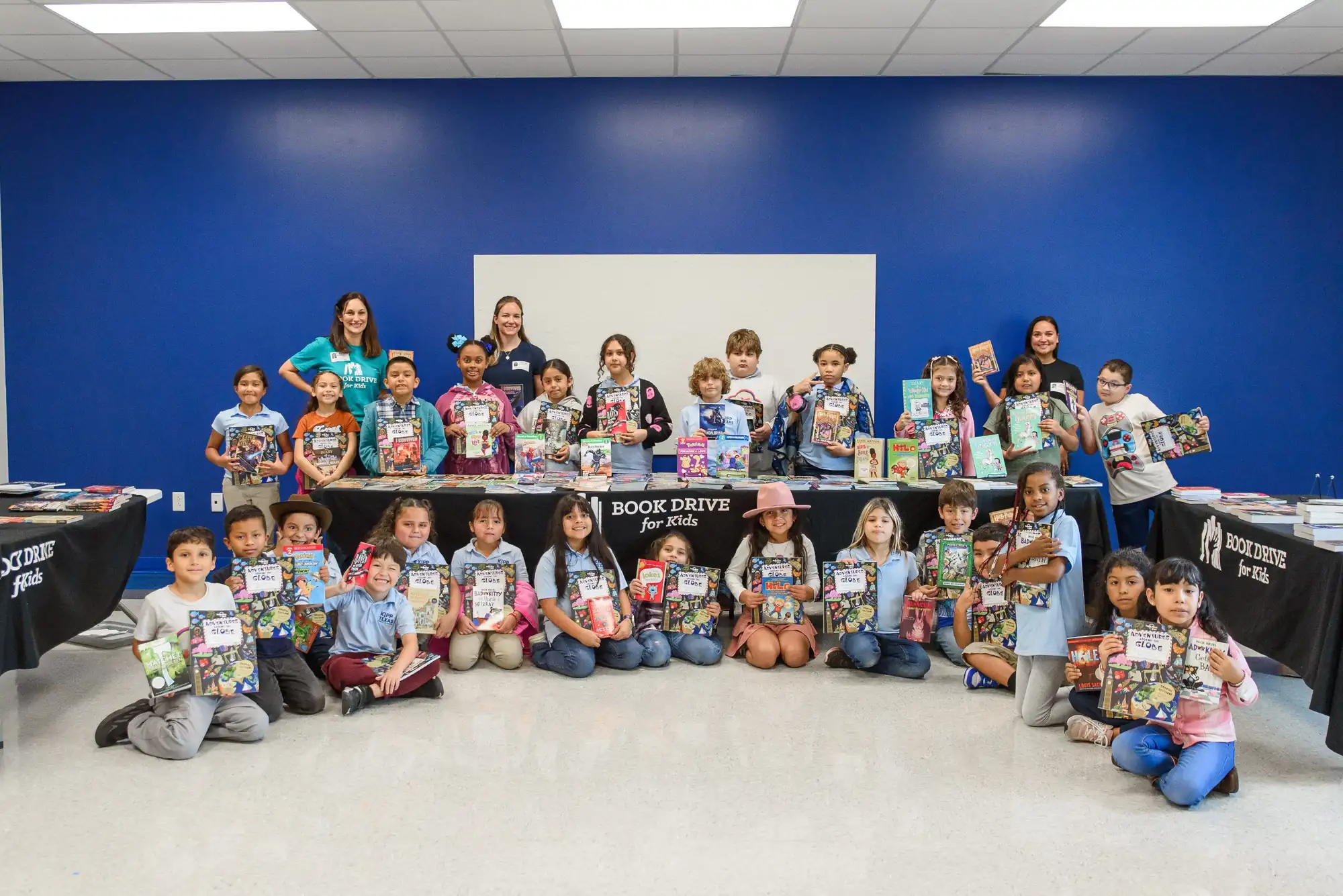 A whole class at KIPP Austin Obras poses with Book Drive for Kids volunteers and tables, every student holding the brand-new book they chose