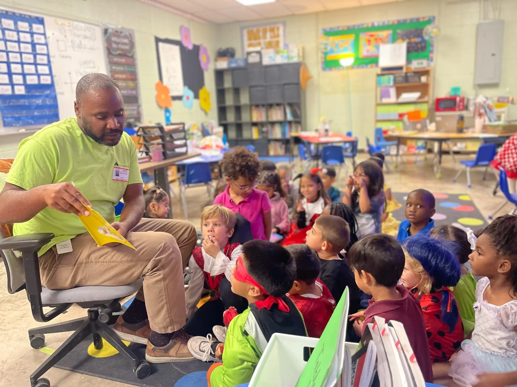 A volunteer reads a picture book aloud to a rapt circle of costumed kindergartners at a free book fair