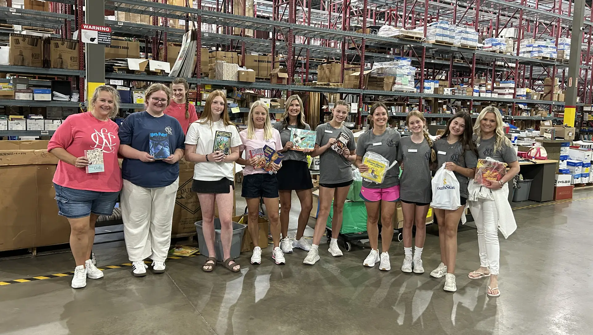 National Charity League volunteers holding books at the Book Drive for Kids warehouse in Lewisville
